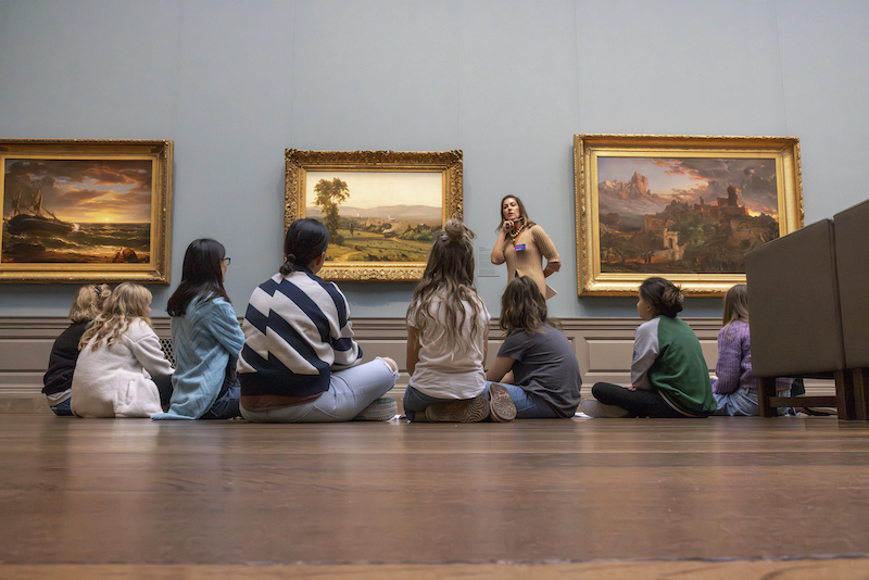 Docent Christie Kramer introduces George Inness' The Lackawanna Valley to a seated group of fifth graders and their parents in gallery 64