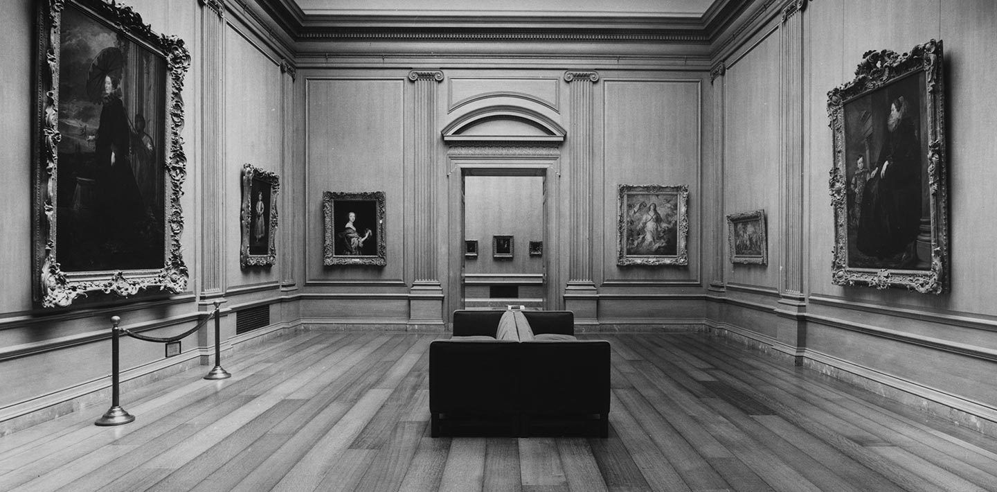 A large gallery stands empty with a large doorway in the center surrounded by paintings
