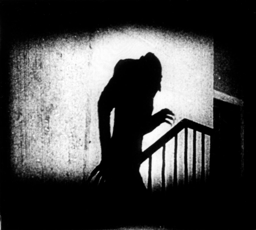 Black and white film still from Nosferatu showing a ghoulish shadowed creature in the shape of a man 