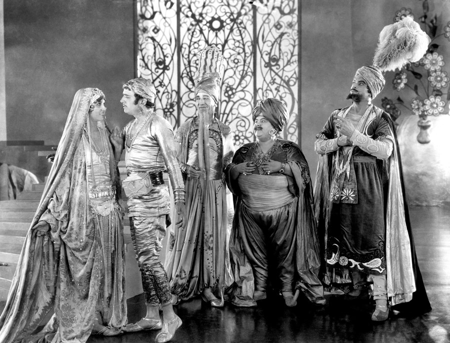 Black and white film still from The Thief of Bagdad showing a man and woman staring into each other's eyes while three men look on in admiration