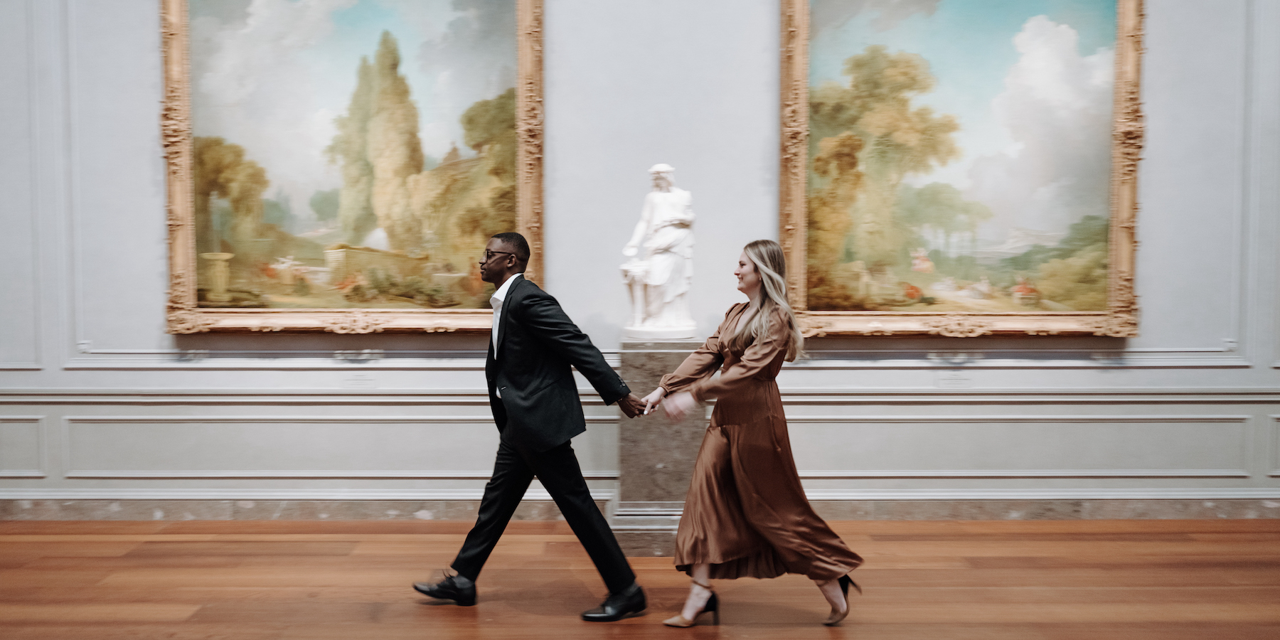 A couple holds hands while strolling through galleries with Fragonard paintings